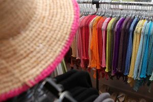 A sun hat int he foreground and in the background, in focus, a rack of colorful shawls